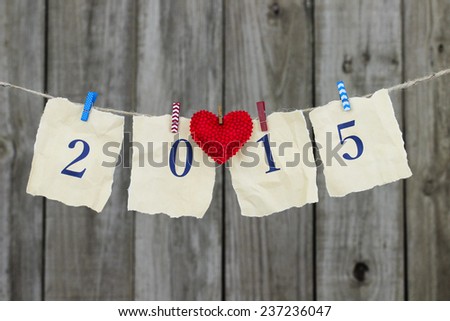 2015 in blue on antique parchment paper sign with red fabric heart hanging on clothesline with wooden background