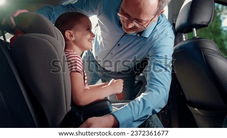Dad puts her Kid girl in car seat safe car. Happy family. Father secures her kid in car seat using child safety belt. Family road trip Dad cares about her daughter safety. Child sits in car child seat Royalty-Free Stock Photo #2372361677