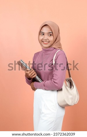 Beautiful young Asian woman holding a laptop while carrying a bag with a smiling face showing teeth