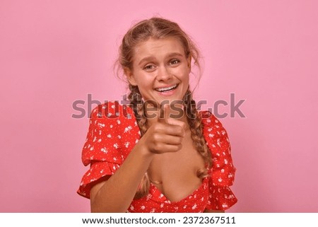Young cheerful casual Caucasian woman millennial laughs and points with finger at screen enjoying funny advertising and laughing at stand-up show or jokes comedian posing on isolated pink background.