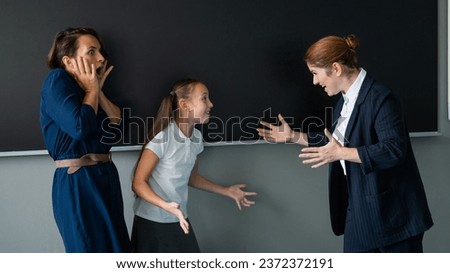 The teacher screams at the schoolgirl and her mother standing at the blackboard.  Royalty-Free Stock Photo #2372372191