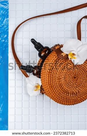 Body oil, orchid, beach woven bag on a pool background. Body care product after the pool. Body lotion mockup with SPF. Cocktail by the pool. Safe tanning oil for body. 