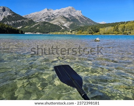 Outdoor watersport recreational image of a black plastic kayak paddle, a clear freshwater lake and a mountain range in the background. Royalty-Free Stock Photo #2372398181