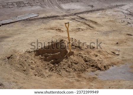 Mountain of sand at a construction site. Foundation material. Soil prepared to strengthen the soil.Shovels in the sand. A shovel got stuck in the sand at a construction site.