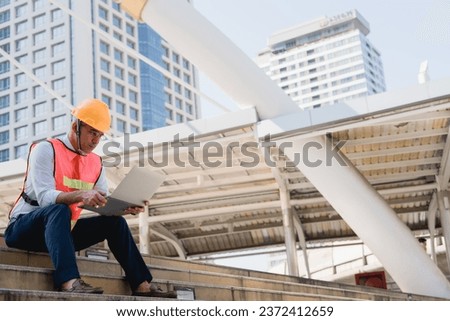 Construction engineer using laptop and sitting outdoor site building working blueprint project, planning project schedule. Thinking problem solving and planning, Engineering and construction concept.