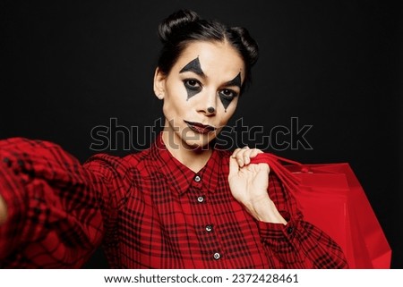 Young woman with Halloween makeup face art mask wear clown costume red dress hold shopping package bags do selfie isolated on plain black background studio. Scary holiday party concept buy day concept