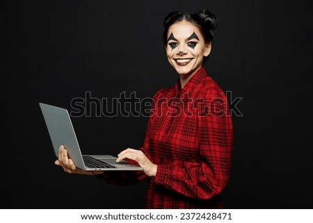Young IT woman with Halloween makeup face art mask wear clown costume red dress work hold using laptop pc computer isolated on plain solid black background studio portrait. Scary holiday party concept