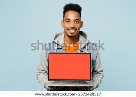Young IT man of African American ethnicity wears denim jacket orange t-shirt hold use work on laptop pc computer with blank screen workspace area isolated on plain pastel light blue cyan background