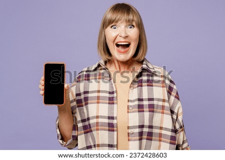 Elderly blonde amazed woman 50s years old wear beige t-shirt shirt casual clothes hold in hand use mobile cell phone with blank screen workspace area isolated on plain pastel light purple background