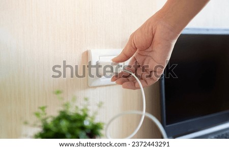 Hand ready to plug or unplug white power cord cable mobile phone charger charts Into electric socket on wall. Electricity charger concept. Royalty-Free Stock Photo #2372443291