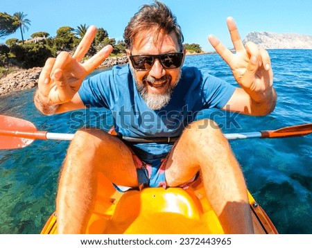 One cheerful man have fun and pose for a crazy picture sitting inside a yellow kayak canoe  with ocean water and coast in background. Happy tourist summer holiday vacation lifestyle people doing tour