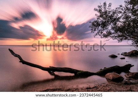 Sunset on Ringkobing Fjord in Denmark at Hvide Sande. Longtime Exposure with a fallen Tree in the foreground. The Water is Smooth an the sky dramatic. Beautiful colors Royalty-Free Stock Photo #2372445465