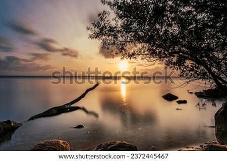 Sunset on Ringkobing Fjord in Denmark at Hvide Sande. Longtime Exposure with a fallen Tree in the foreground. The Water is Smooth an the sky dramatic. Beautiful colors Royalty-Free Stock Photo #2372445467