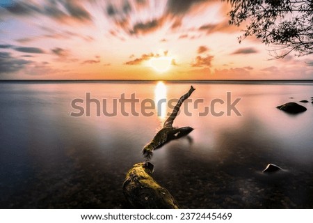 Sunset on Ringkobing Fjord in Denmark at Hvide Sande. Longtime Exposure with a fallen Tree in the foreground. The Water is Smooth an the sky dramatic. Beautiful colors Royalty-Free Stock Photo #2372445469