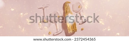 Happy New Year and Christmas holiday banner, sparkling wine champagne bottle, wine glasses on pink background, copy space. Cute dwarf in sequins hat as xmas bottle decor, shadow, bokeh, star filter