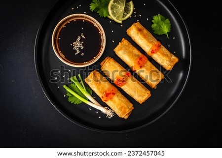 Vegetable filled spring rolls and soy sauce on black wooden table  Royalty-Free Stock Photo #2372457045