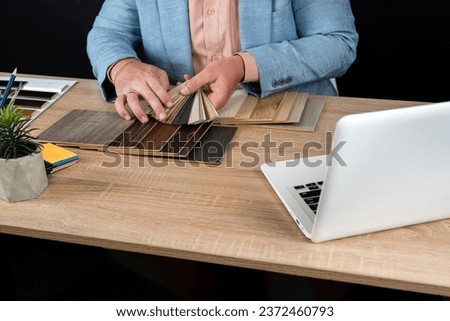 Designer hand choosing wood texture laminate  in catalog at office desk, laptop pen and notepad.  Catalog guide for interior architecture