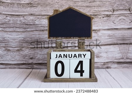 Chalkboard with January 04 calendar date on white cube block on wooden table.
