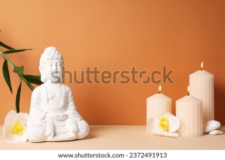 Buddha statue, candles, flowers and stones on orange background, space for text