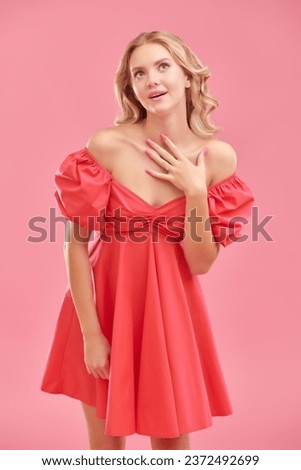 Young beauty. A cute attractive girl with blond hair poses in a pink dress and smiles. Pink studio background. Femininity, beauty and fashion.
