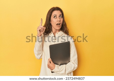 Middle-aged woman with laptop on yellow having some great idea, concept of creativity.