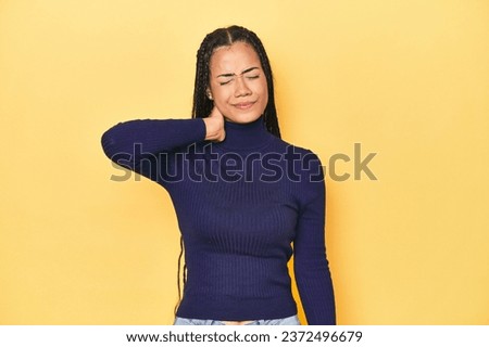 Young Indonesian woman on yellow studio backdrop having a neck pain due to stress, massaging and touching it with hand.