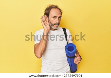 Man with yoga mat in yellow studio trying to listening a gossip. Royalty-Free Stock Photo #2372497901
