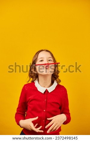 Funny teen school girl make mustache on her face with red pencil, back to school concept, comedy expression, copy space