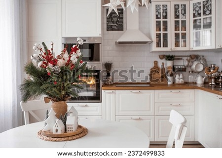 A spruce bouquet with red berries, toys, cotton on a white kitchen table. Christmas decorations in the interior. The concept of preparation for the New Year's holiday 2024.