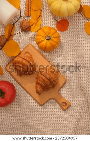 Fabric background with wooden tray of delicious croissants decorated with autumn leaves, pumpkins and walnuts. Top view, empty space for design. Advertising photo