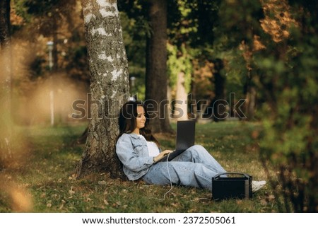 A woman in nature works on a laptop charging from a portable charging station Royalty-Free Stock Photo #2372505061