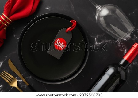 Black Friday Feast: Overhead view of plates, "sale" price label, lavish gold cutlery, red napkin in ring, wine bottle, glass on black marble backdrop