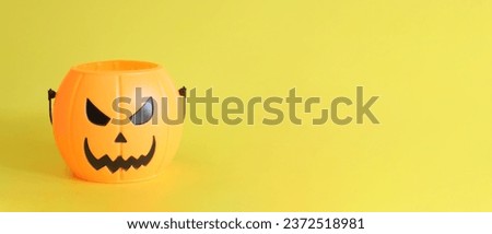 Happy Halloween. Plastic pumpkin bucket with an evil smiling on a yellow background, empty space for text. Copy space. Banner for Halloween Royalty-Free Stock Photo #2372518981
