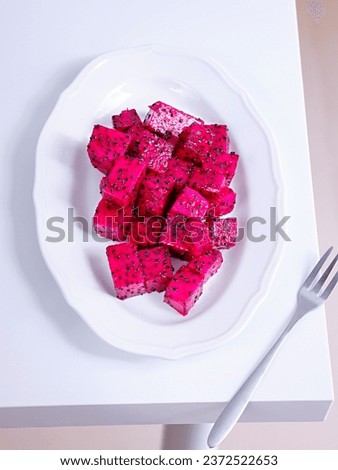 A vertical shot of pink dragon fruit cut in cubes in a white plate with a fork on a table