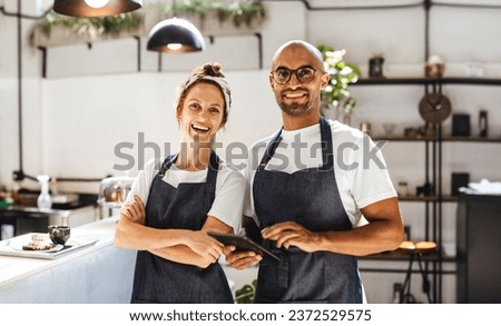 Two hospitality entrepreneurs standing in their small coffee shop. Successful man and woman working as a team to manage the day-to-day operations and provide excellent service to their customers. Royalty-Free Stock Photo #2372529575
