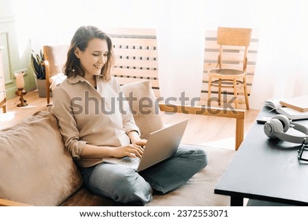 Vivacious Woman in the Living Room. Typing on Laptop with Energy A vivacious woman is typing on a laptop, sitting on the sofa in the living room. Sofa Workstation. Energetic Woman Typing on Her Laptop Royalty-Free Stock Photo #2372553071