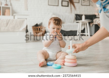 Beautiful young mother plays and teaches her baby 6 months old on the floor in the living room.mom and baby play with toys Royalty-Free Stock Photo #2372564415
