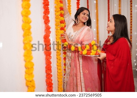 An Indian girl and her sister decorate their house with marigold flowers - an Indian festival, Diwali celebration. Two beautiful girls dressed in ethnic wear for the festival of Diwali  Royalty-Free Stock Photo #2372569505