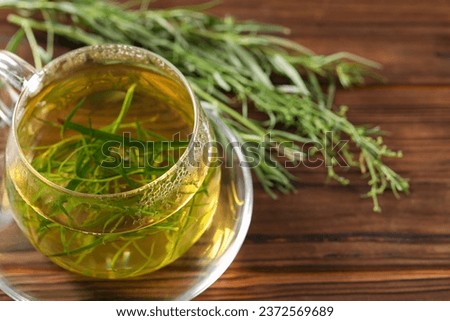 Cup of homemade tarragon tea on wooden table, closeup. Space for text Royalty-Free Stock Photo #2372569689