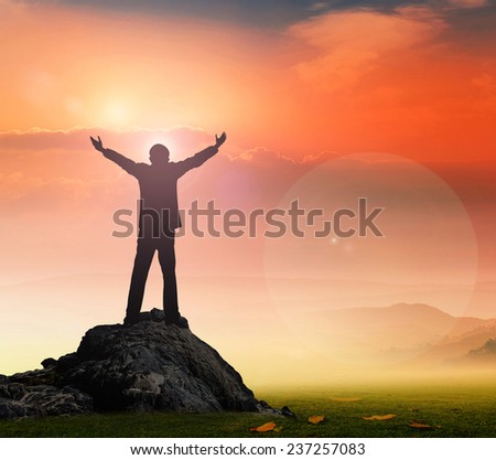 Thank God concept: Silhouette of businessman with hands raised to beautiful autumn sunset background