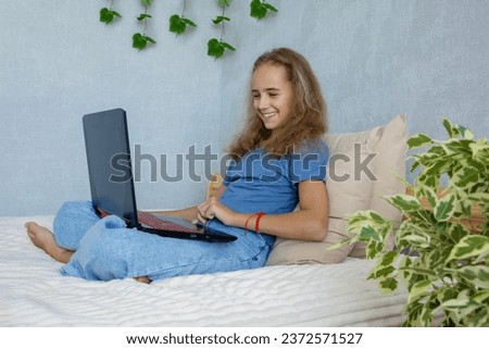 A cute teenage girl is undergoing online training sitting at home on a bed with a laptop. The concept of home education.