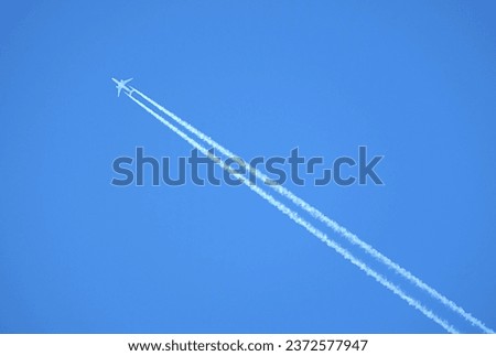 Large two engine passenger supersonic airplane flying from right to left high in blue cloudless sky leaving long white track Royalty-Free Stock Photo #2372577947