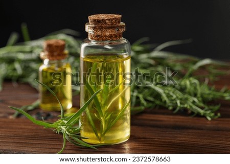 Bottles of essential oil and fresh tarragon leaves on wooden table, closeup. Space for text Royalty-Free Stock Photo #2372578663