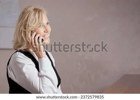 Blonde receptionist talks with customer that all the rooms are busy in luxury hotel. Female worker reserves nice hotel suite via smartphone Royalty-Free Stock Photo #2372579835