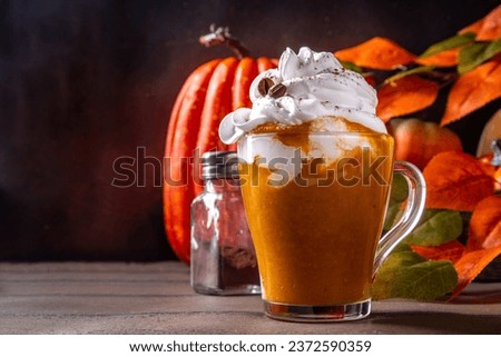 Pumpkin spice latte in a glass cup, with a lot of whipped cream and coffee beans decor 