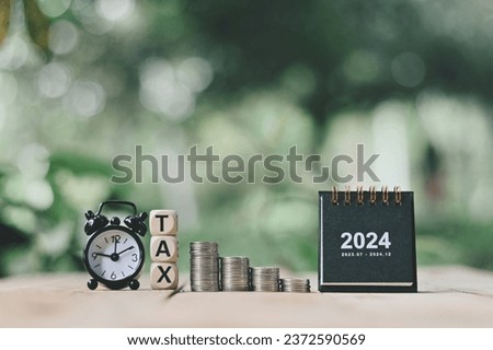 close up stack of coin, 2024 small calendar, wooden tax text and alarm clock on wood table, saving and manage money to success business, planning cash for holiday season concept Royalty-Free Stock Photo #2372590569