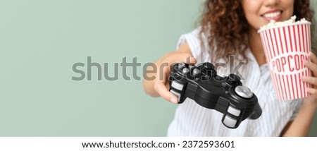 African-American teenage girl with popcorn playing video game on grey background, closeup. Banner for design