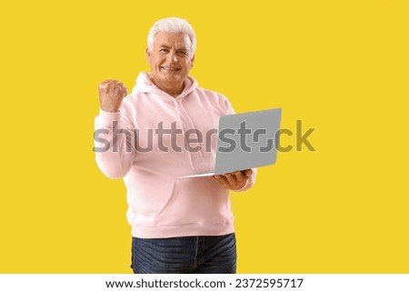Happy senior man with laptop on yellow background