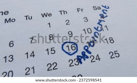 Circle marked date 16 with blue pen ink on a white calendar page with appointment word written in personal handwriting near the day. Closeup macro top view.