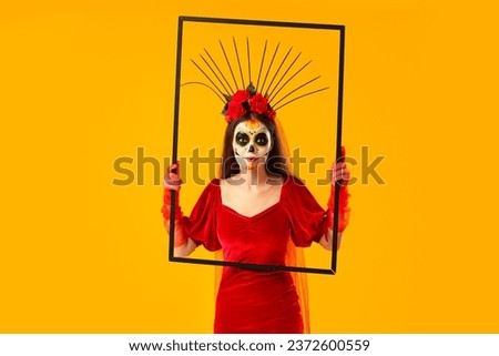 Young woman with painted skull and frame on yellow background. Mexico's Day of the Dead (El Dia de Muertos) celebration